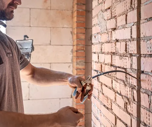Electrician care taie un cablu nou tras prin peretele de cărămidă
