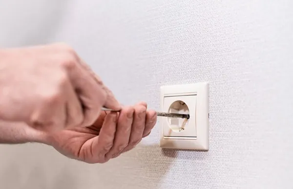 Mâini care strâng cu șurubelnița o priză nouă în perete